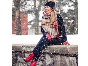A women sitting on a stone wall with her red sound boots on in a winter wonderland.  Boots go great with jeans for a casual fun look.